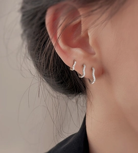 Close-up of three stacked silver wavy earrings with small diamonds on a model's ear