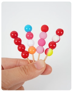 Gros plan de miniatures de fruits confits en résine tenues à la main sur fond blanc