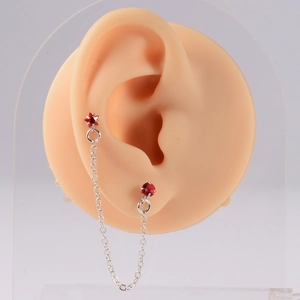 Macro view of silver ear stud with red star gemstone and chain link on ear model