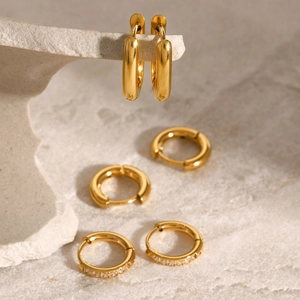 Three pairs of golden stainless steel hoop earrings with crystal inlay on stone surface