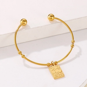 Detail of gold-plated open cuff bracelet with embossed charm on white steps background