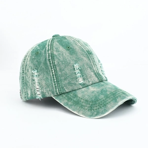 Close-up side view of a vintage washed green denim baseball cap with distressed frayed details
