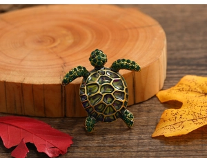 Detailed close-up of a turtle brooch with green rhinestones and enamel shell on wood