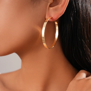 Close-up of stylish wide flat-edge golden hoop earrings on model with metallic finish