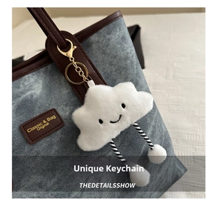 Close-up of a plush white cloud charm with a smiley face on a blue denim tote bag