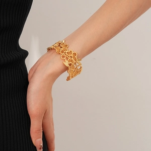 Detailaufnahme eines vergoldeten Armreifs mit hohlem Blumendesign am Handgelenk einer Frau