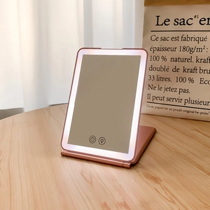 Macro view of portable rose gold LED makeup mirror with folding stand on wooden surface