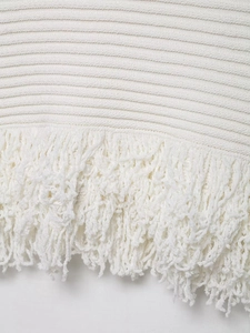 Detail of white knit dress featuring horizontal texture and fringe trim at the hem