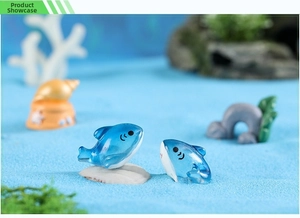 Miniature blue resin whale figurines on blue sand with seashells and coral decor