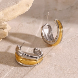 Modern two-tone C-shape stud earrings in silver and gold steel on stone background
