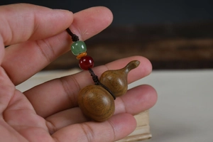 Close-up of a carved rosewood gourd keychain with colorful beads and woven cord detail