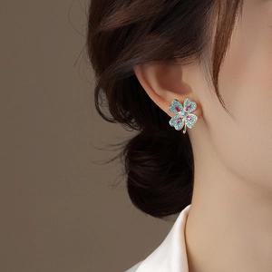 Gros plan d'une boucle d'oreille trèfle avec pierres bleues et gemme rouge sur l'oreille