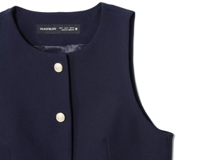Détail de l'encolure de gilet sans manches bleu foncé avec boutons dorés et labels