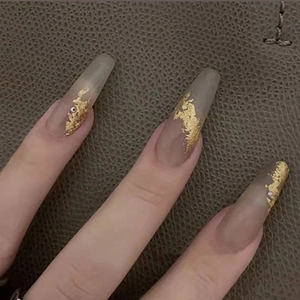 Detail of long ballerina press-on nails with gold foil and rhinestones on nude base