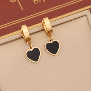 Close-up of golden huggie earrings with black heart charms on a beige velvet texture
