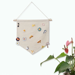 Beige canvas banner hanging on wall displaying enamel pin collection with wooden rod