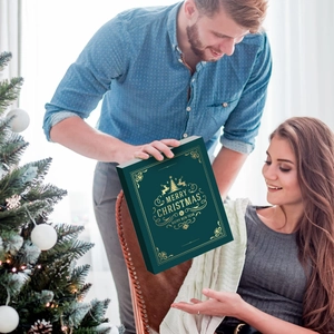 Uomo regala un calendario dell'Avvento verde a forma di libro a una donna vicino all'albero