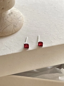 Macro shot of square red zircon stud earrings with silver pins on a minimalist pedestal