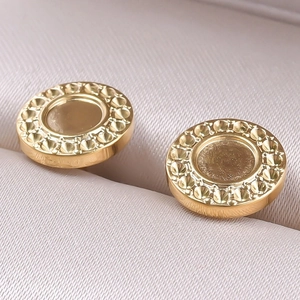 Detailed macro view of gold round stud earrings with textured edges on jewelry cushion