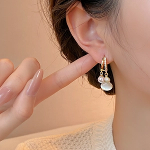 Elegant gold earrings with pearls and zircon opal pendants worn by a female model