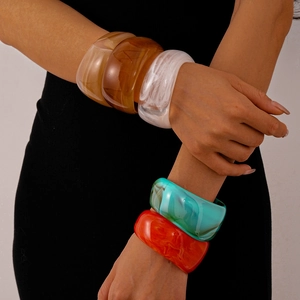 Wide geometric acrylic bangles in marble and amber colors worn by a model