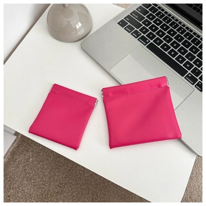 Close-up of rose red leather mini pouches in two sizes on a minimalist white desk