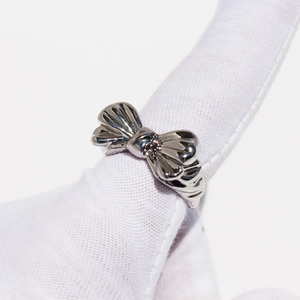 Polished silver metal bow ring with pleated design shown on a gloved finger on white