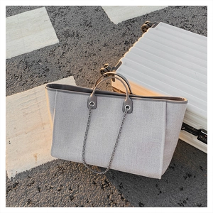 Close-up of light grey canvas tote bag with chain strap leaning on a suitcase outdoors
