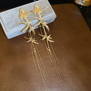 Detail view of gold bamboo leaf earrings with long metal tassels on a jewelry box