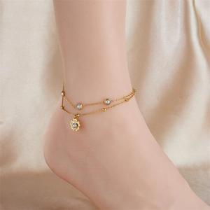 Double-layered gold anklet with pearl accents and flower pendant on a silk background