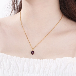 Close-up of model wearing a delicate gold chain necklace with a purple strawberry pendant