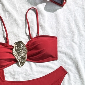 Detail of red bikini with gold metal oyster buckle on white textured fabric background