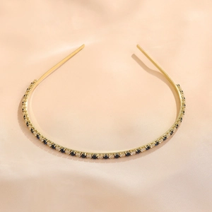 Close-up of golden headband with emerald and white cubic zirconia on silk background