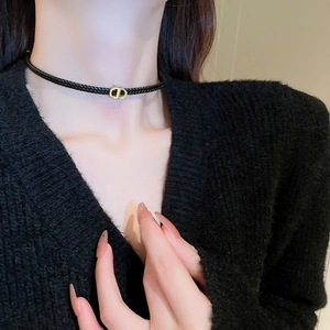 Detail of woven black leather choker with a gold-tone CD letter charm on neck