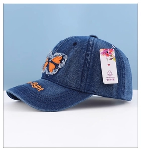 Detail of dark blue denim baseball cap with butterfly embroidery and frayed edges