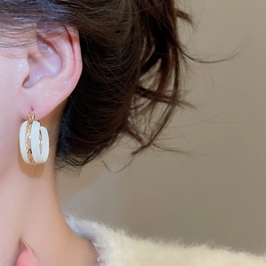 Close-up of a wide C-shaped gold and white enamel hoop earring worn by a model