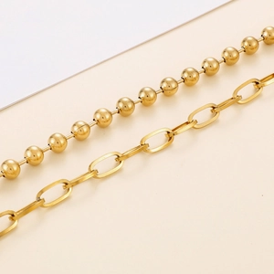 Collier en acier inoxydable doré avec perle et pendentif cœur sur fond beige minimaliste