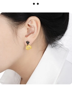 Close-up of irregular black and gold stud earring with inset diamond on model's ear