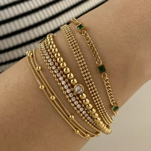 Detail view of gold beaded bracelets and Cuban link chain with green emerald accents