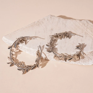 Detail of silver hoop earrings with delicate leaf charms resting on a textured stone