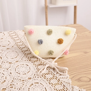 Close-up of cream woven straw bag with colorful pom poms on a lace table runner