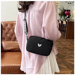 Detail of black nylon crossbody bag with silver butterfly and lettered wide strap