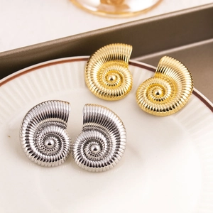 Golden and silver spiral conch stud earrings displayed on a white ceramic plate