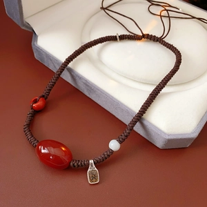 Detail of adjustable wax cord necklace with red agate bead and engraved metal pendant