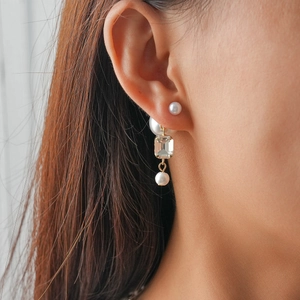 Close-up of elegant pearl drop earrings with rectangular crystal in gold finish