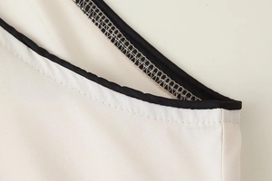 Détail de la robe sans manches blanche montrant le passepoil noir et la couture fine