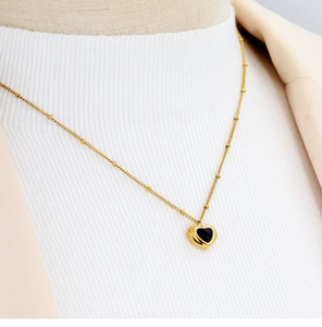 Detail shot of a gold heart pendant necklace with black onyx on a white sweater