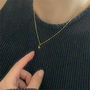 Close-up of minimalist gold star pendant necklace worn over a black ribbed sweater