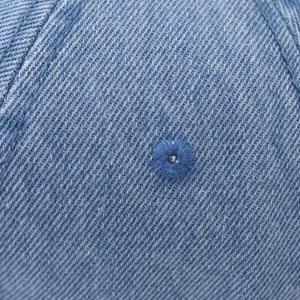 Macro shot of light blue washed denim fabric with detailed twill weave and stitched eyelet