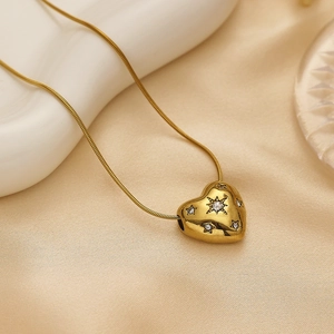 Macro detail of gold heart pendant with star engraving and zircon on silk fabric